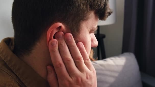自宅のソファに座って痛みを伴う頭部に触れる耳の痛みを持つ病気の若い原因アジアの男性の閉鎖側のビュー 痛みを伴う中毒に苦しむ30代の不健康な男 ヘルスケアと耳鳴りの概念 — ストック動画