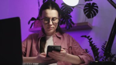 Gözlüklü, kendine güvenen, uzaktan kumandalı kadın masadaki arama dosyalarında ev kablosuz ağıyla bilgisayardan bilgisayara oturuyor. Akıllı genç bayan kullanıcı senkronizasyonu iki aygıt kullanarak veriyi yeniden yükler