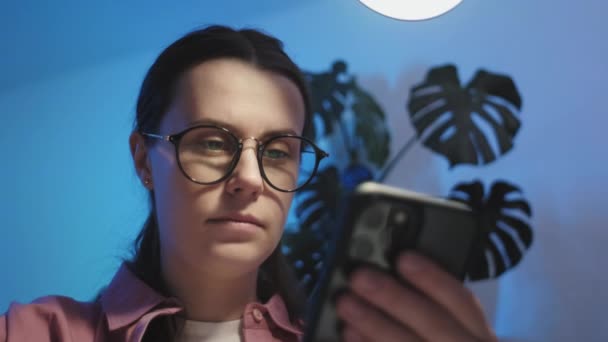 有选择地聚焦在专注于眼镜的高加索女人上 深夜工作 看智能手机信息 网上冲浪信息 休闲和现代技术 新的移动应用 等待呼叫概念 — 图库视频影像