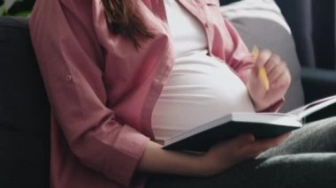 Seçici odak noktası, rüyadaki genç hamile kadının evdeki kanepede oturup günlüğe yazması. Kadın, sağlığı ve müstakbel anne olma deneyimini kişisel not defterinde tanımlar. Hamilelik ve eğlence konsepti