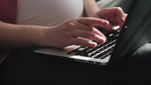 妊娠中の女性の選択的な焦点は 自宅から快適なソファの上に座って 大きな腹で屋内でラップトップを入力し オンラインアプリを使用して チャット インターネット上でのショッピング 医師に相談します フリーランスのコンセプト — ストック動画