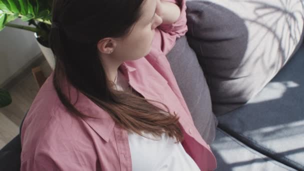 近距离观察20多岁忧心忡忡的高加索孕妇独自坐在沙发上感受压力和焦虑的情景 年轻的孕妇在想即将出生的孩子 — 图库视频影像
