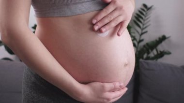 Evdeki güzel göbeğine cilt bakımı yapan hamile bir kadın. Göbek anne göbek nemlendirici kremini evde dururken hafifçe göbek derisine sürterken. Hamilelik konsepti