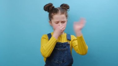 Sıradan kıyafetler giyen küçük kızın portresi pis ve iğrenç bir koku alıyor, katlanılmaz bir koku, nefesini burnunda tutuyor, mavi arka planda izole edilmiş. Kötü koku konsepti