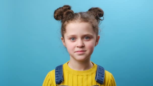 近距离拍摄了一个微笑的小女孩的头像 快乐而漂亮的孩子在工作室的蓝色背景墙上摆出孤身一人的姿势 8岁的孩子看着相机 人的情感概念 — 图库视频影像