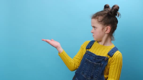 困惑的小女孩穿着迷惘的衣服 手牵着手 用手掌摆出停下的姿势 在工作室的蓝色背景墙上摆出隔离的姿势 并留有复制的空间 童年生活方式概念 — 图库视频影像