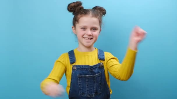 快乐可爱有趣的小女孩舞动着紧握的拳头 挥动着胜利的手势 在工作室的蓝色背景墙上摆出孤立的姿势 童年生活方式和人的情感概念 — 图库视频影像