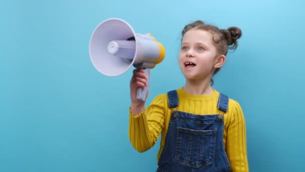 漂亮的小女孩用扩音器说话 宣布新闻 大声宣布广告 用扩音器发出警告 在蓝色的背景下显得孤立无援 童年生活方式概念 — 图库视频影像