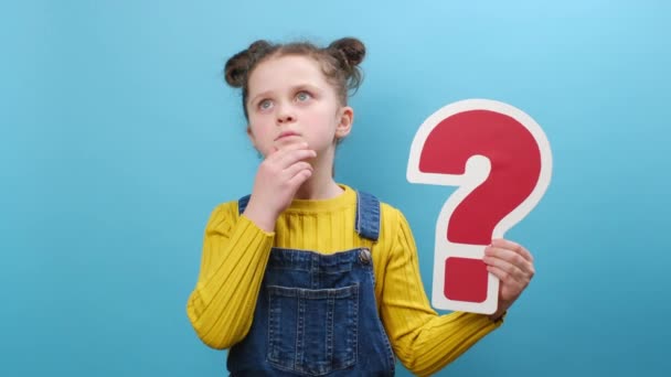赤のクエスチョンマーク記号を保持8歳の小さな女の子の子供の肖像画は スタジオで青の背景色の壁の上に隔離されたポーズを混乱の中でヤシを発生させます 子供のライフスタイルのコンセプト — ストック動画