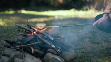 Bahar ya da yaz günü kamp ateşinde ekmek yapan tanınmayan turistlerin yakın çekim görüntüleri. Gezgin ormanda yemek pişiriyor. Kamp ortamı ve açık hava yaşam tarzı konsepti