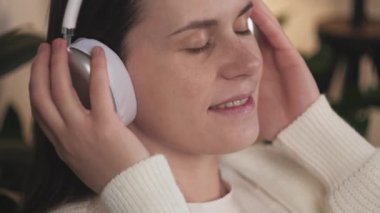 Dikkatli, mutlu, beyaz, kablosuz kulaklık takan, rahatlatıcı müzik dinleyen, evdeki rahat koltukta dinlenen, ilginç sesli kitapların keyfini çıkaran, boş zamanlarını evde geçiren bir kadın.