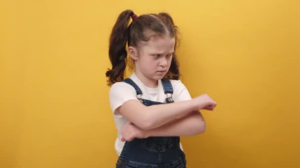 ポートレート悲しい不幸な小さなでこぼこの女の子の子供が腕を組んでポーズを取り カメラを見て 気分が悪くなり スタジオで黄色の背景色の壁の上に隔離されたポーズ いじめの被害者 — ストック動画