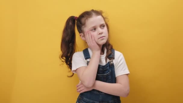 沮丧的小女孩靠在手上 看着镜头 厌烦而冷漠的表情 对交流不感兴趣 在黄色的工作室背景下装出孤独寂寞的样子 童年概念 — 图库视频影像