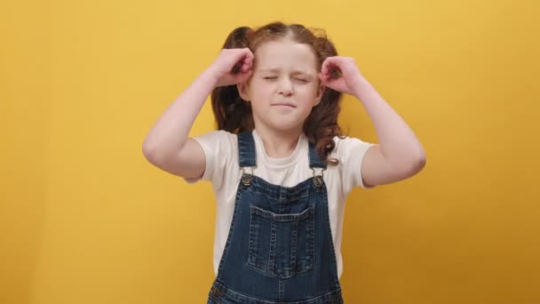 惊喜交集的小女孩面容惊愕地展示了手部脑爆裂的姿势 在工作室的黄色背景墙上显得孤立无援 人的情感概念 — 图库视频影像