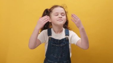 Mutlu küçük bir kız portresi rahatlıyor, gülümsüyor gözleri kapalı küçük bir çocuk huzurlu bir nefes alıyor, hoş bir koku alıyor, sarı arka plan duvarında izole edilmiş bir poz veriyor.