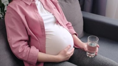Kablosuz kulaklıklarla gülümseyen genç ve güzel bir kadın evdeki rahat koltukta oturmuş müzik dinliyor ve oturma odasında bir bardak tatlı su içiyor. Hamilelik ve melodi terapisi konsepti