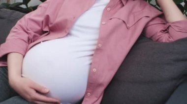 Kablosuz kulaklık takan, evde rahat bir koltukta oturmuş, müzik dinleyen, sağlıklı ve kolay hamileliğin tadını çıkaran, çekici, beyaz, hamile bir kadın. Hobi, stressiz konsept