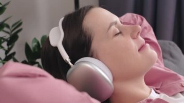 Modern kablosuz kulaklıklı barışçıl gülümseyen kadını kapat rahat koltuğa otur müzik dinle, kulaklıklı mutlu sakin kadın kanepede dinlen, kaliteli sesin tadını çıkar. Stressiz konsept