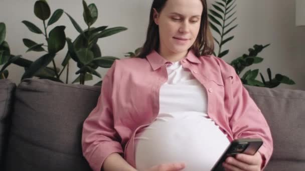 Lachende Jonge Blanke Zwangere Vrouw Met Behulp Van Mobiele Telefoon — Stockvideo