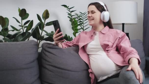 Joven Mujer Embarazada Alegre Con Auriculares Utilizando Teléfono Móvil Haciendo — Vídeo de stock