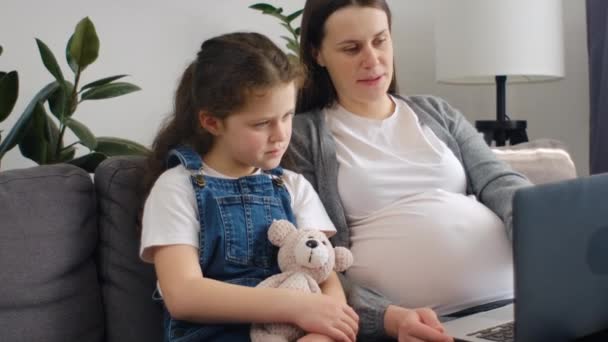 Opiekuńcza Młoda Ciężarna Matka Uroczą Córeczką Siedzi Kanapie Używając Laptopa — Wideo stockowe