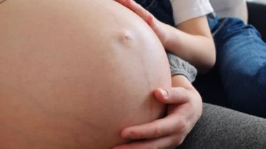 Genç, hamile bir anne ve kızı sevmek, rahat bir koltukta oturmak, büyük bir göbek okşamak, sevgi ve ilgi göstermek, çocuk doğurmayı beklemek, şefkati hissetmek, evde tek başına dinlenmek. Annelik kavramı