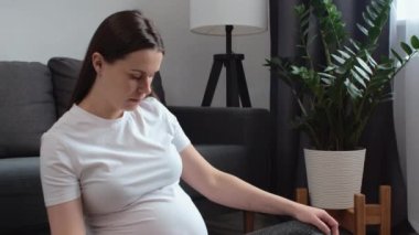 Hamile genç bir kadın evdeki hafif oturma odasında rahat bir paspasın üzerinde rahat ve yumuşak yoga egzersizleri yapıyor. Hamilelik yogası, fitness, meditasyon ve sağlıklı yaşam tarzı konsepti