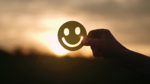 背景驚くべき日没や日の出に黄色の幸せな笑顔の顔を保持する男性の手の選択的な焦点 良いフィードバック評価と肯定的な顧客レビュー 満足度調査 精神健康評価 — ストック動画