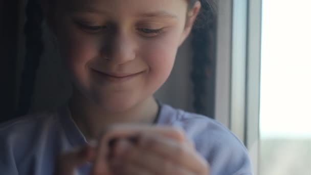 用智能手机 在家里的窗台上玩网络游戏 把漂亮的小女孩的照片合拢起来 新一代和现代技术的过度使用 父母控制的概念 — 图库视频影像