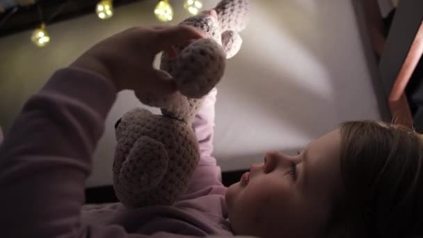 抱着可爱的学龄前小女孩躺在温暖的毛毯下 抱着玩具熊舒服的枕头上 睡个好觉 快乐祥和的小女孩在床上享受着周末懒散的夜晚 — 图库视频影像