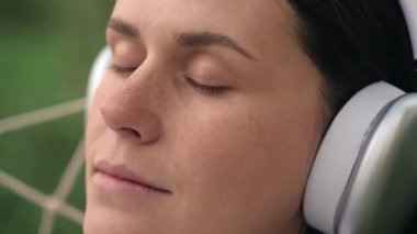 20 'li yaşlarda rahat bir hamakta uzanmış, kablosuz kulaklık takmış, hafta sonu boyunca en sevdiği şarkıyı ve güzel bahar doğasını dinleyen rahat ve çekici genç bir kadın.