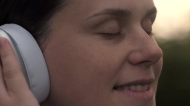 Gün batımında, güzel bahar veya yaz ormanlarında müzik dinleyen, kulaklık takan huzurlu, mutlu genç bir kadın. Dikkatli, sakin, çekici, 20 'li yaşlarda beyaz bir kadın favori şarkının tadını çıkarıyor.