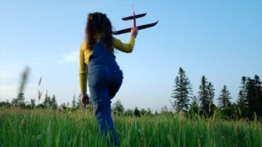 Gün batımında oyuncak uçakla sahada koşan mutlu küçük kız çocuğunun silueti. Çocuklar mavi arka planda oyuncak uçak oynuyorlar. Uçma ve pilot olma hayalleri. Yavaş çekim