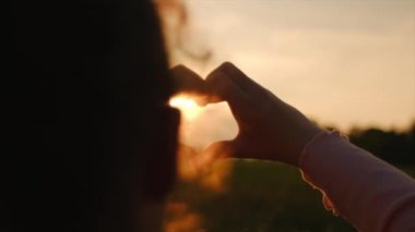 Arka planda elleri ile kalp yapan küçük bir kız çocuğu silueti inanılmaz bir günbatımı. Neşeli çocuk, içinde gün doğumu olan ellerinden kalbini gösteriyor. Seyahat, turizm ve tatil konsepti. Yaz tatili