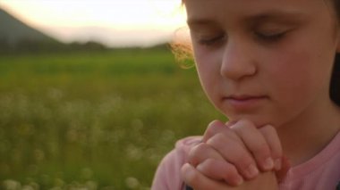 Güzel çocuk gün batımında dua ederek inancını ve bağlılığını ifade eder. Küçük şirin Hıristiyan ve dua ederken mutlu. Gözleri kapalı ve elleri katlanmış genç bir kız Tanrı 'yla masumca konuşuyor.