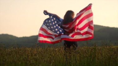 Küçük kız 4 Temmuz 'da, Amerika' nın Bağımsızlık Günü 'nde güneşli yaz günbatımında kutlama yapıyor. Ülke bayrağını tutan gururlu Amerikalı çocuk. Amerika Birleşik Devletleri bayrağıyla yeşil alanda küçük bir çocuk.