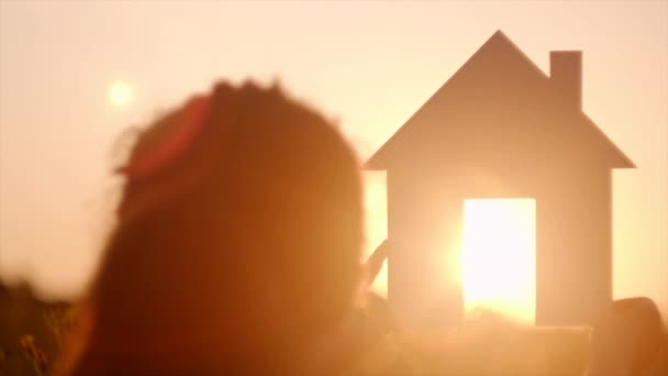 在背景温暖的日落下 小女孩手持纸制房屋模型的特写侧视图 在夏日的大自然中 在灿烂的阳光下回家 梦想自己的房子 住房和抵押贷款概念 有选择的重点 — 图库视频影像