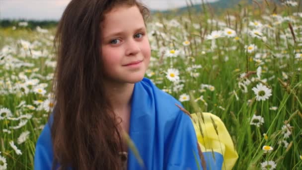 美しい夏の山を背景に緑のフィールドに立って ウクライナのフラグに包まれた愛国的な美しい少女の肖像画穏やかな夕日 独立記念日お祝い選挙のコンセプト — ストック動画