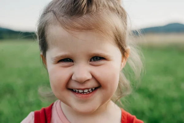 stock image Close up portrait of cheerful pretty little girl child smiling looking at camera, enjoying summer vacation in park on background mountains at warm sunset. People emotion, weekend and nature concept