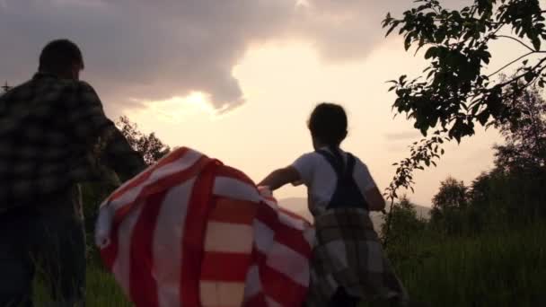 在史诗的日落中 年轻父亲和可爱的小女儿带着美国国旗漫步在高山上 自由而自豪的独立爱国家庭感受到了自由的概念 慢动作 — 图库视频影像