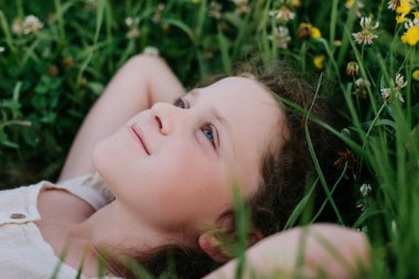Rahatlamış, gülümseyen küçük bir kızın portresi. Yaz günü taze yeşil çimenlerin üzerinde yatıyor. Tasasız, güzel, çocukluk çağında bir çocuk sahada uzanıyor ve hafta sonunun tadını çıkarıyor. Doğa ve çocukluk kavramı