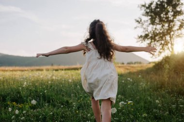 Arka plandaki dağlarda koşan mutlu küçük kız ve gün batımında ya da gün doğumunda gökyüzü. Çocuk kollarını bir uçağın kanatları gibi kaldırarak koşuyor, çocukluk hayali tatili. Çocuk rüyası, uçak pilotu