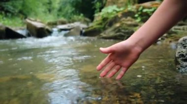 Sakin yaz mevsiminde çocuk elinin dağ suyuna dokunuşunu kapat. Bütünsel ve çevreye duyarlı yaşam tarzı kavramı. Doğada berrak ve temiz su. Doğal kaynakların korunması