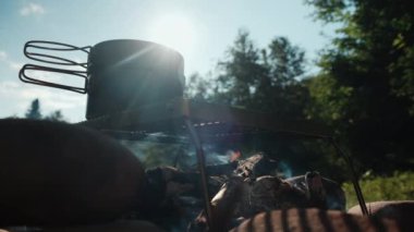 Arka plandaki kamp ateşinin üzerinde kaynamış su ve güzel sıcak bir sabahta mavi gökyüzü. Yaz mevsiminde şenlik ateşi. Yürüyüş kavramı. Kamp havası ve açık hava yaşam tarzı.