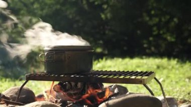 Güzel bir sabah vakti, arka plan yeşili üzerinde, siyah bir tencerede kaynayan suya yakın durun. Yaz mevsiminde şenlik ateşi. Macera, seyahat ve yürüyüş kavramı. Hızlı yemek kampı.