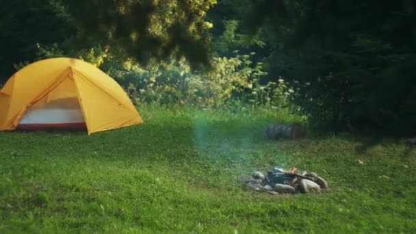在美丽的云杉森林附近的绿色草地上 有一个黄色的旅游帐篷和篝火 夏令营的自然背景在夏令营 积极的生活方式 自由和户外概念 — 图库视频影像