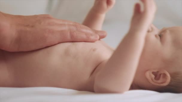 爸爸的小手按摩宝宝的特写 新生儿皮肤护理的概念 预防结肠炎 男性手按摩新生儿 漂亮的高加索婴儿躺在舒适的床上 慢动作 — 图库视频影像