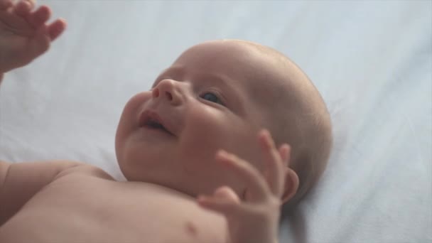 一个可爱的微笑的白人男婴的画像 他有一双蓝眼睛 四个月大 躺在舒适的床上 可爱的新生儿笑着休息 快乐的童年生活 年轻一代的观念 — 图库视频影像