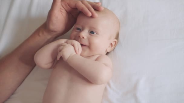 爱的父亲在清晨轻柔地抚摩着快乐可爱的小宝宝 抚摩着小儿子 笑着新生儿躺在舒适的白色床上在家里 爱情和家庭的概念 — 图库视频影像