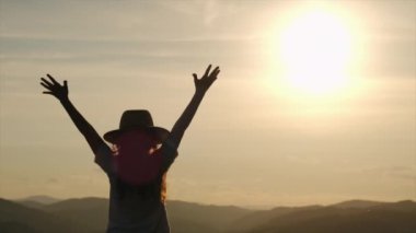 Şapkalı mutlu küçük çocuğun seçici odağı gün batımında ellerini dağın arka planına kaldırıyor. Çocuk yaz günü aktif bir hafta sonunun tadını çıkarıyor. Konsept seyahat, çocukluk, macera. Yavaş çekim